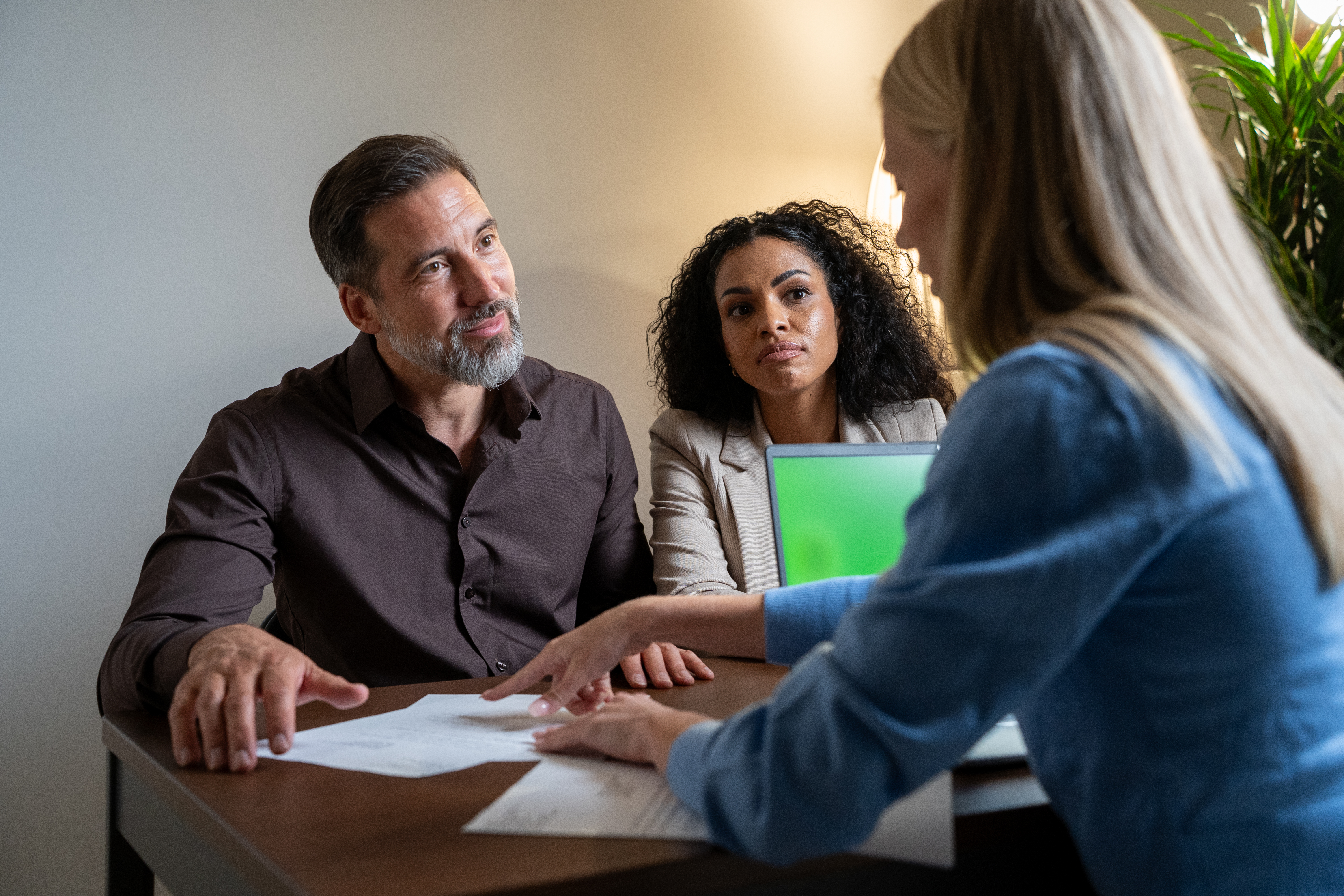Diverse couple meets with a professional advisor in an office to review documents and sign a contract, formalizing an agreement during a private business meeting at a desk.